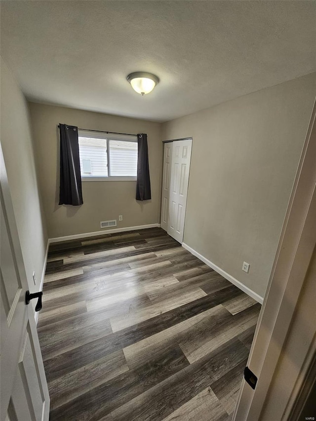 unfurnished bedroom featuring dark wood finished floors, baseboards, visible vents, and a closet