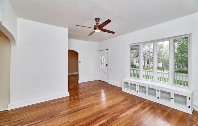 interior space featuring arched walkways, hardwood / wood-style flooring, baseboards, and ceiling fan
