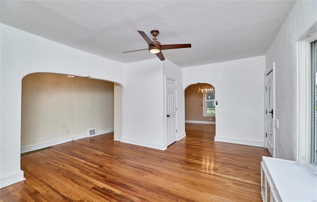 empty room featuring visible vents, baseboards, arched walkways, ceiling fan, and wood finished floors