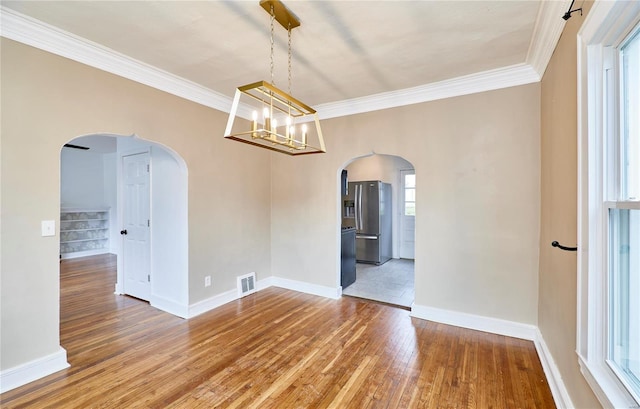 unfurnished dining area with arched walkways, visible vents, hardwood / wood-style flooring, and ornamental molding