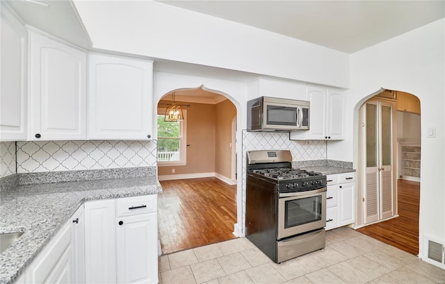 kitchen featuring arched walkways, visible vents, baseboards, and appliances with stainless steel finishes