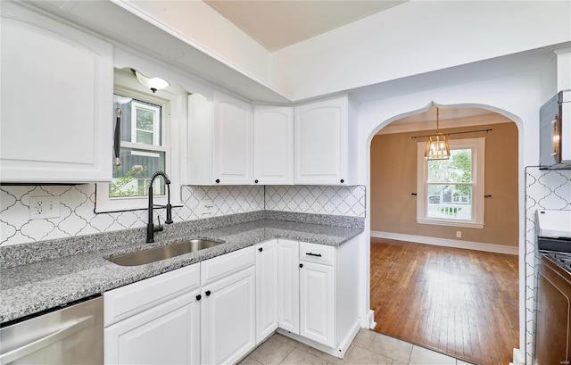 kitchen with tasteful backsplash, baseboards, arched walkways, a sink, and stainless steel dishwasher