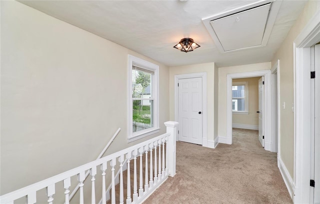 hall featuring light carpet, attic access, baseboards, and an upstairs landing