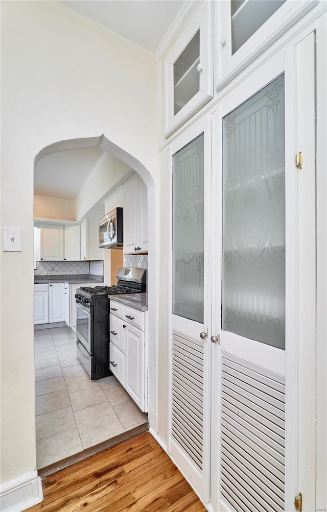 kitchen with glass insert cabinets, arched walkways, white cabinetry, stainless steel appliances, and backsplash