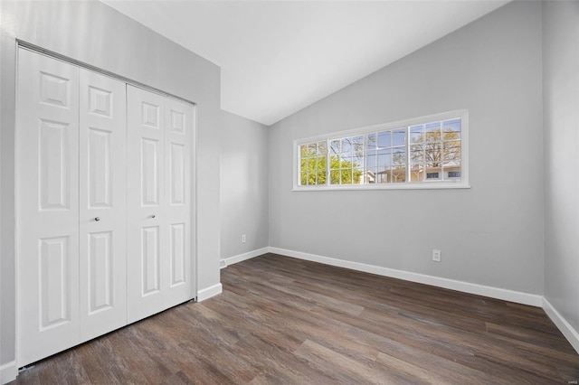 unfurnished bedroom with a closet, baseboards, wood finished floors, and vaulted ceiling