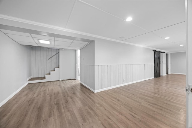 finished basement with stairs, a barn door, a paneled ceiling, and wood finished floors