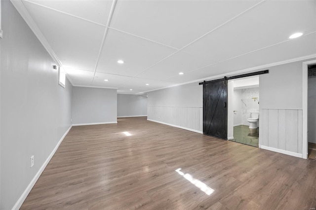 basement with wainscoting, wood finished floors, ornamental molding, and a barn door