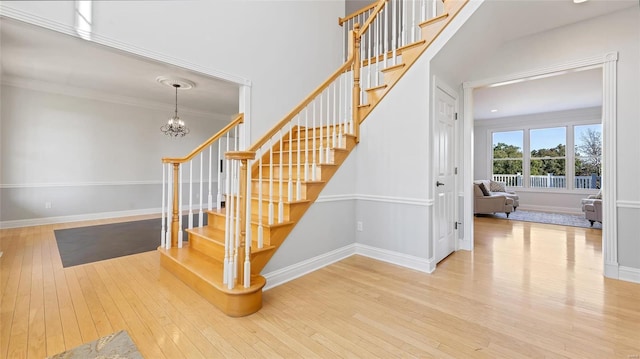 staircase featuring baseboards, ornamental molding, an inviting chandelier, and wood-type flooring