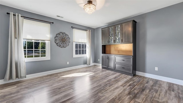 spare room featuring baseboards, visible vents, a healthy amount of sunlight, and wood finished floors