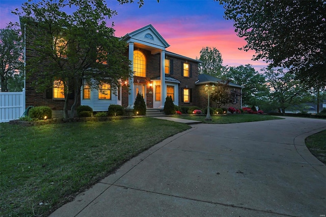 view of front facade with a front lawn, fence, curved driveway, and brick siding