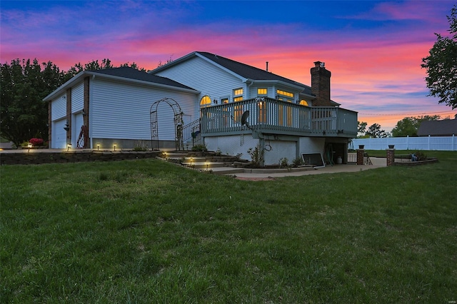 back of house at dusk with a lawn, a deck, fence, and a chimney