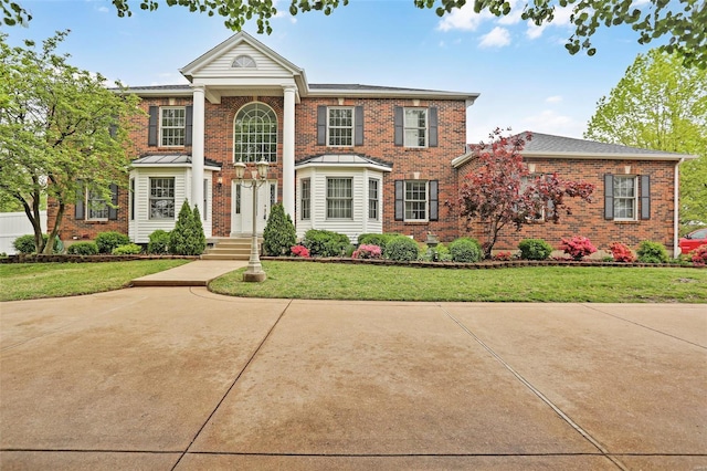 greek revival inspired property with a front lawn and brick siding