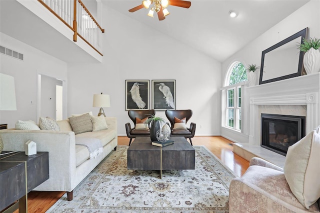 living area with a fireplace, ceiling fan, high vaulted ceiling, visible vents, and wood finished floors
