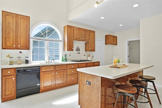 kitchen featuring a sink, brown cabinets, a kitchen breakfast bar, black appliances, and light countertops
