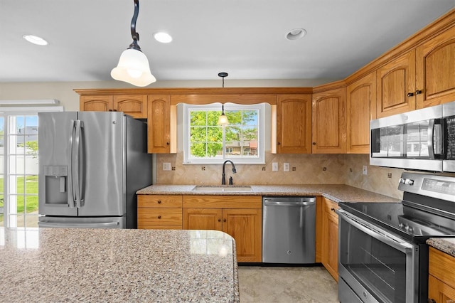 kitchen featuring light stone counters, a sink, appliances with stainless steel finishes, backsplash, and hanging light fixtures