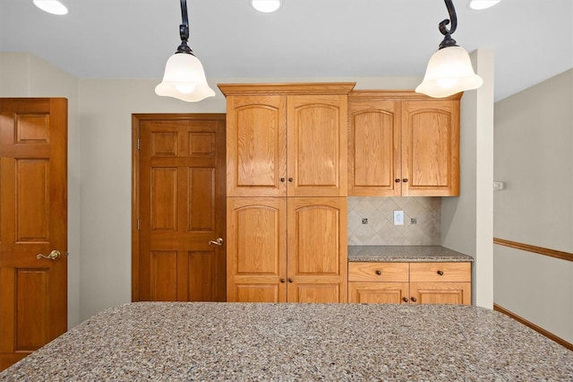 kitchen featuring light stone counters, backsplash, and decorative light fixtures
