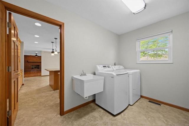washroom featuring laundry area, a ceiling fan, washing machine and dryer, a sink, and baseboards