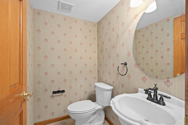 bathroom with a sink, toilet, baseboards, wallpapered walls, and visible vents
