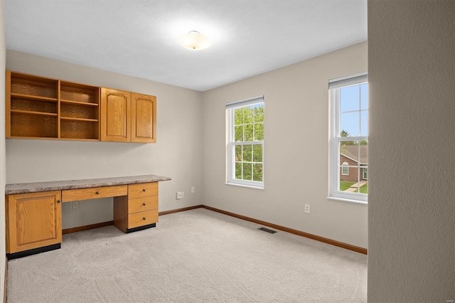 unfurnished office featuring baseboards, light colored carpet, built in desk, and visible vents