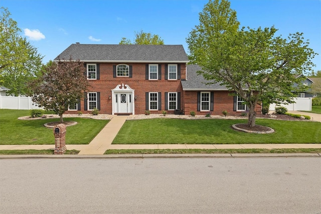 colonial house with brick siding, fence, and a front lawn