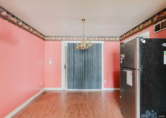 unfurnished dining area featuring an inviting chandelier, baseboards, visible vents, and wood finished floors