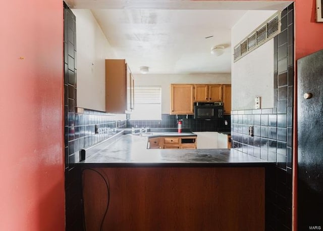 kitchen featuring a sink, a peninsula, black microwave, and backsplash