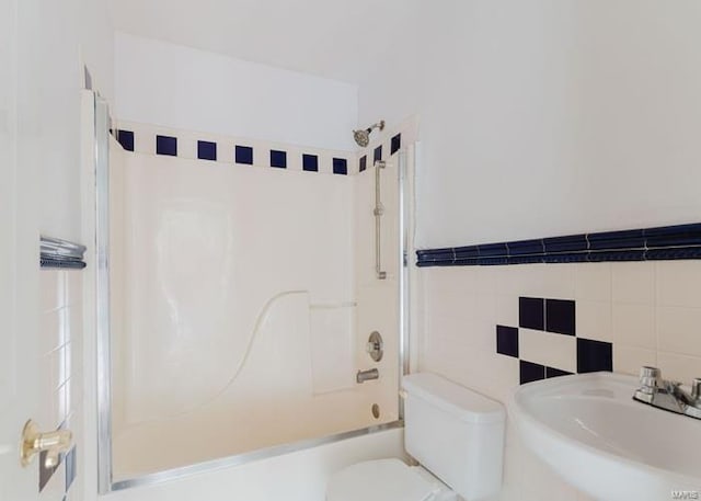 bathroom featuring tile walls, toilet, shower / bathtub combination, and a sink