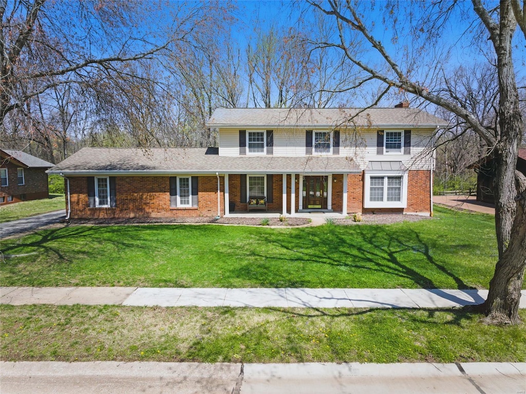 view of front of house featuring brick siding, a front lawn, and covered porch