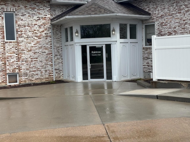 entrance to property featuring brick siding, fence, and a shingled roof
