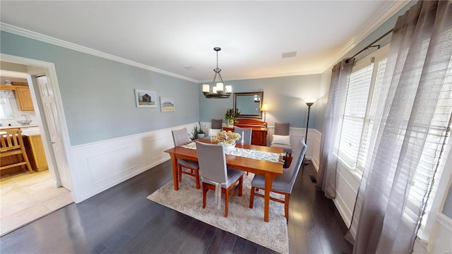 dining room featuring a chandelier, a healthy amount of sunlight, wood finished floors, and wainscoting