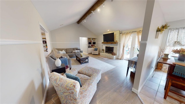 living area featuring baseboards, track lighting, a fireplace, light wood-style floors, and beamed ceiling