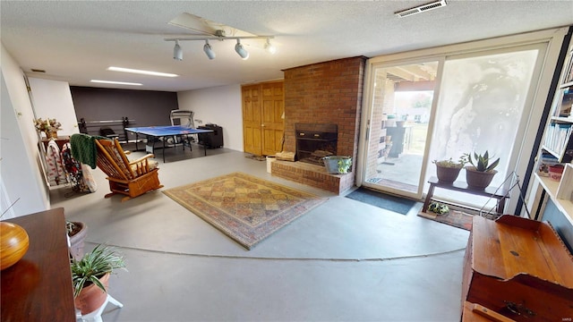 living area with a brick fireplace, visible vents, a textured ceiling, and finished concrete flooring