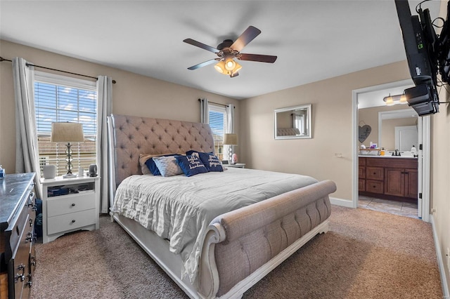 bedroom featuring ceiling fan, connected bathroom, light carpet, a sink, and baseboards
