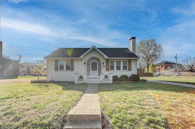 view of front of house with brick siding, a front lawn, a shingled roof, and a chimney