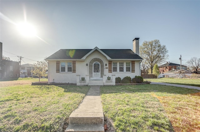 view of front of house featuring a shingled roof, brick siding, a chimney, and a front lawn