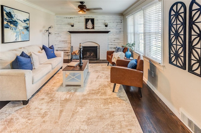 living area featuring baseboards, crown molding, visible vents, a brick fireplace, and wood finished floors