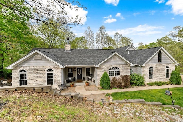 exterior space featuring a front yard, a chimney, covered porch, stone siding, and roof with shingles