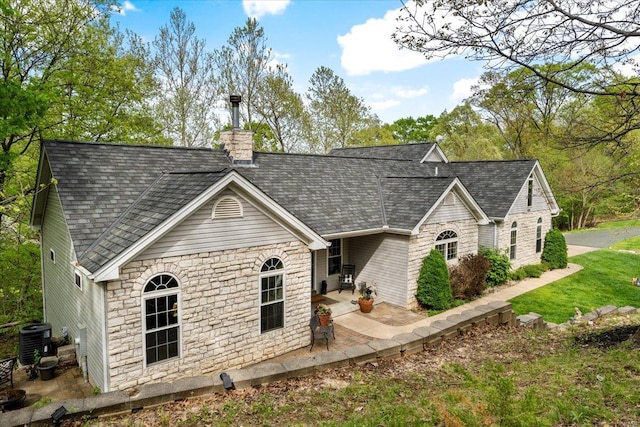 view of front of house with cooling unit, a chimney, a patio area, and stone siding
