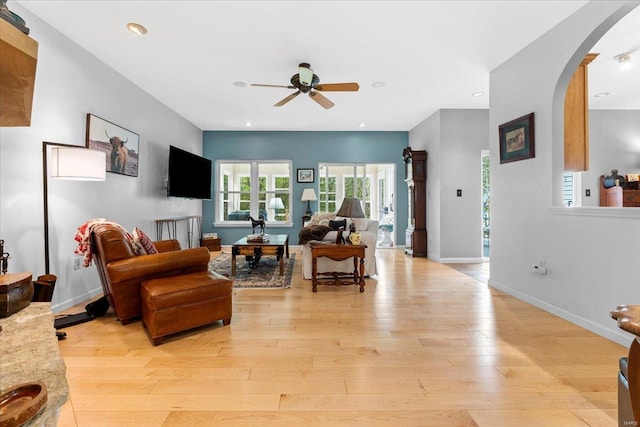 living room with baseboards, arched walkways, light wood-type flooring, recessed lighting, and a ceiling fan