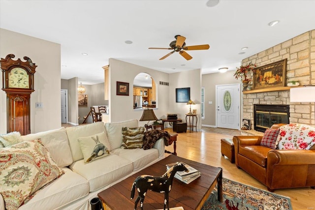 living area featuring baseboards, ceiling fan, a stone fireplace, and light wood finished floors