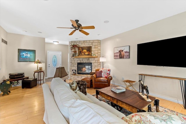 living room with ceiling fan, a stone fireplace, light wood-style flooring, and visible vents