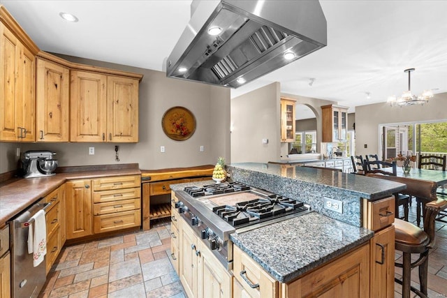 kitchen featuring wall chimney range hood, a breakfast bar area, appliances with stainless steel finishes, a center island, and an inviting chandelier