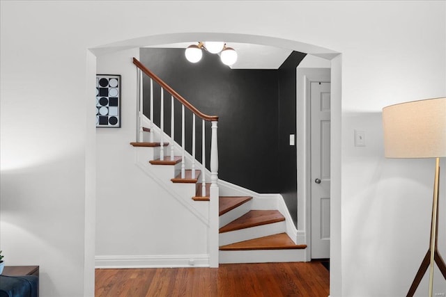 stairs with arched walkways, baseboards, and wood finished floors