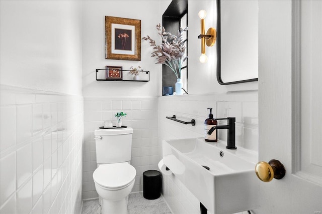 bathroom featuring toilet, tile walls, a sink, and a wainscoted wall