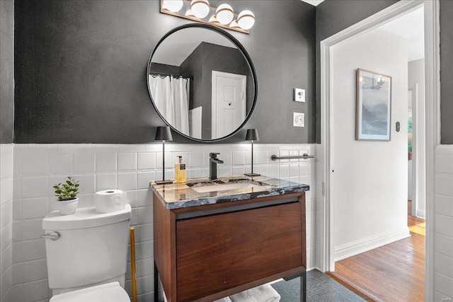 bathroom with vanity, toilet, a wainscoted wall, tile walls, and wood finished floors