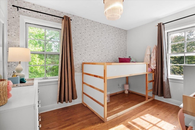 bedroom with multiple windows, wallpapered walls, and wood finished floors