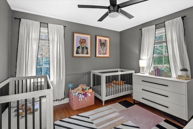 bedroom featuring a ceiling fan, a crib, and wood finished floors