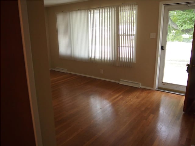 spare room featuring baseboards, a baseboard heating unit, wood finished floors, and visible vents
