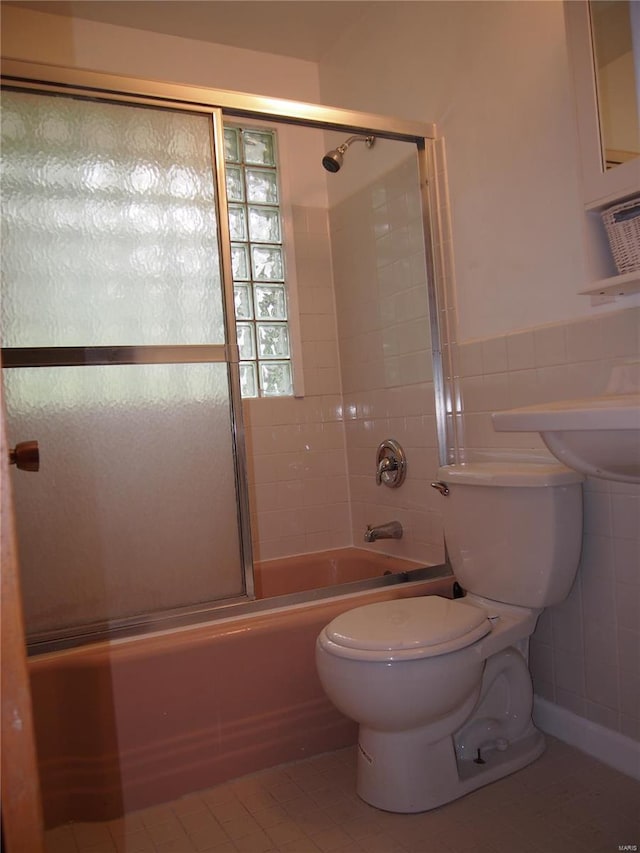 full bath featuring wainscoting, toilet, tile walls, tile patterned floors, and combined bath / shower with glass door