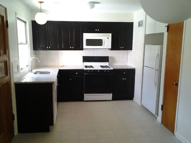 kitchen featuring a sink, dark cabinets, backsplash, and white appliances